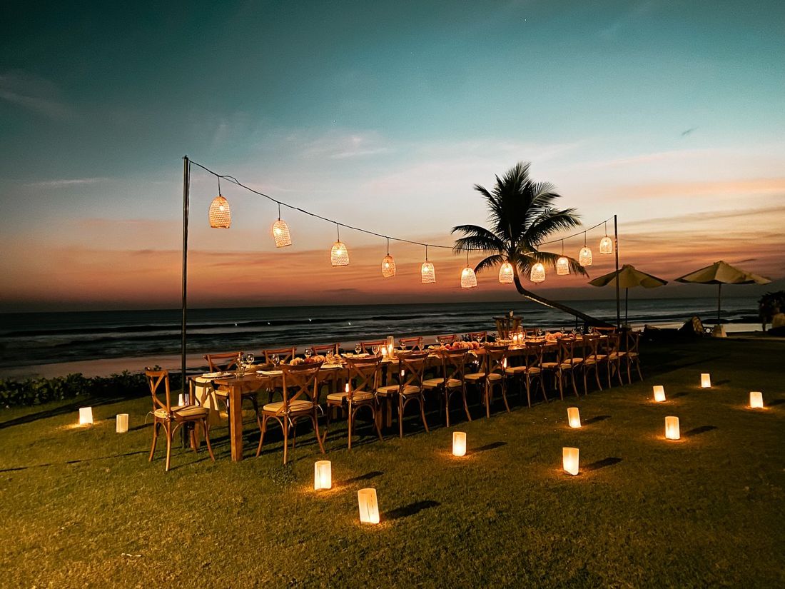 Long dinner table on the lawn under lanterns at sunset